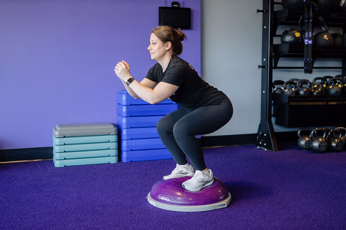 Anytime Fitness Coach demonstrating a BOSU squat stability exercise.