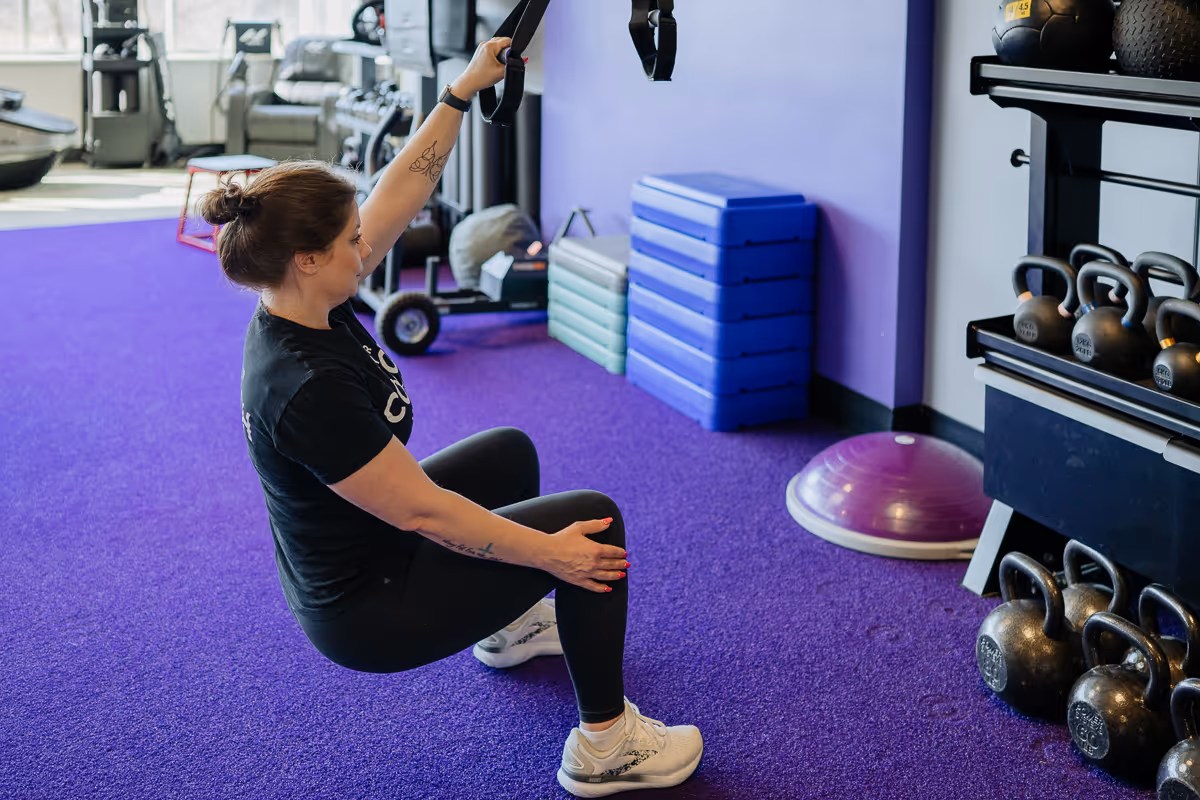 Anytime Fitness Coach using a TRX strap to do a one-arm pull-up in a gym setting.