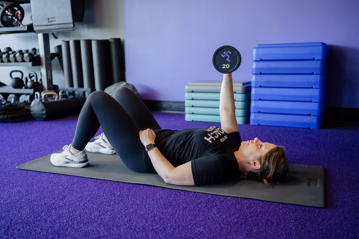 Anytime Fitness Coach demonstrating a single-arm dumbbell chest press on the purple turf.