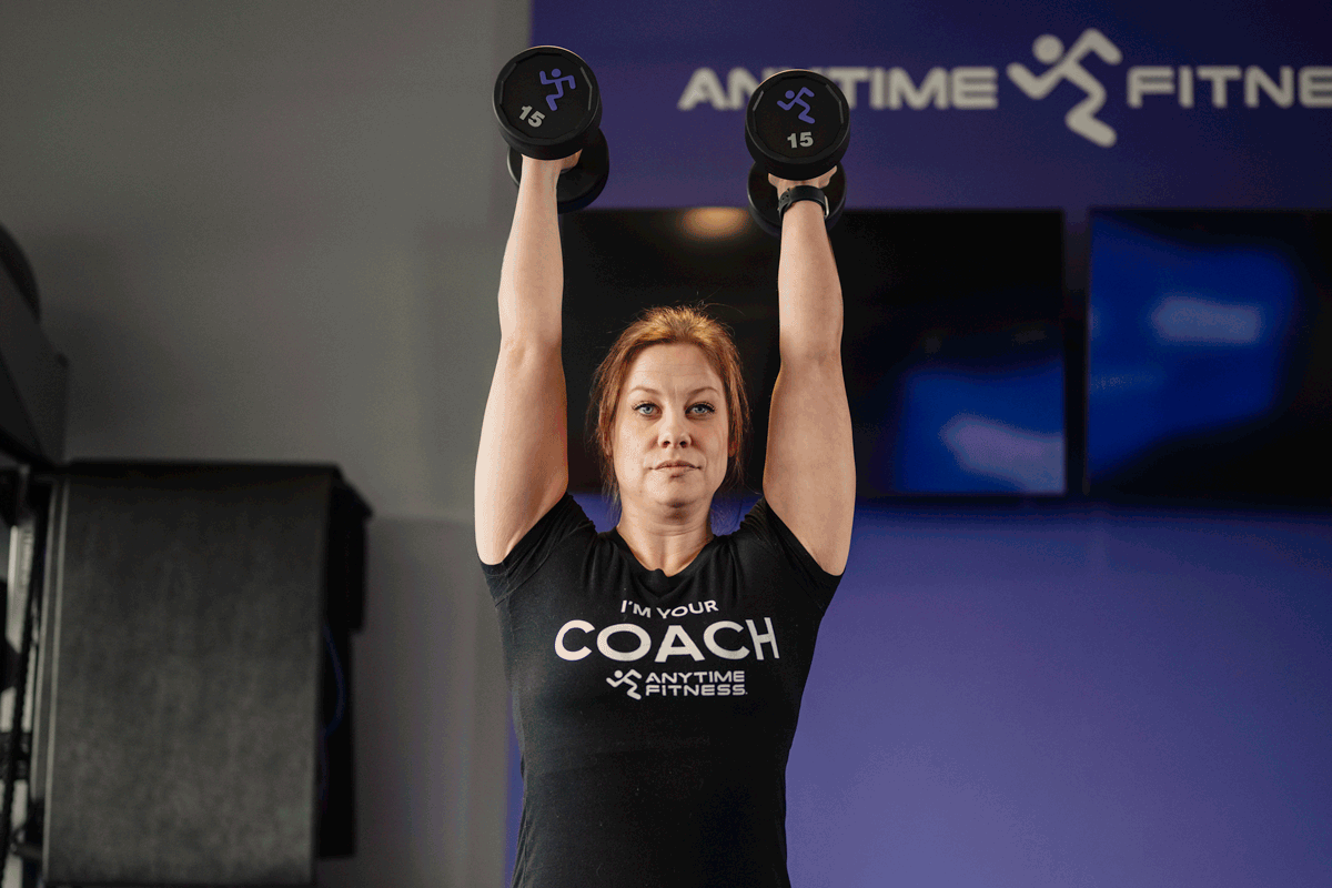 Anytime Fitness Coach demonstrating a dumbbell overhead press.