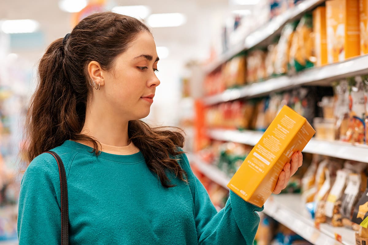 Woman in a supermarket reading a food label, learning how to read nutrition labels for weight loss.