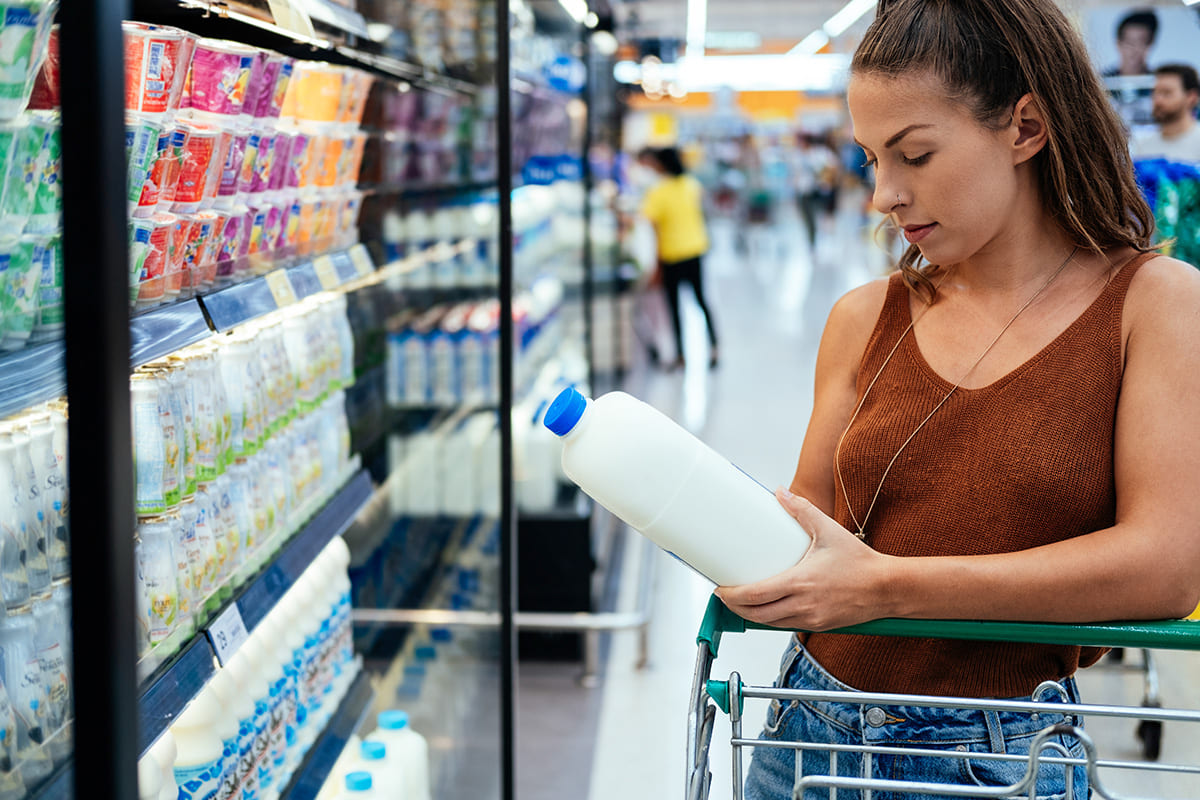Woman in a supermarket reading a nutrition label on a milk jug.
