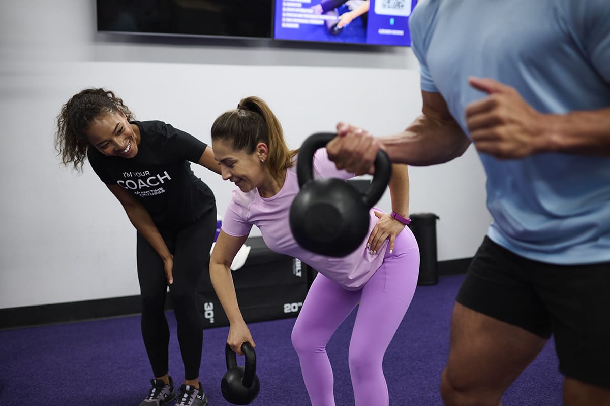 Anytime Fitness Coach working with members in a group workout, demonstrating a kettlebell exercise.
