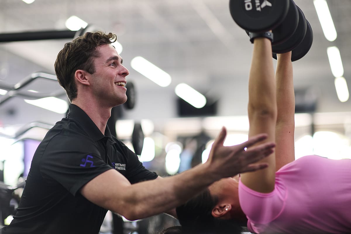 Anytime Fitness Coach spotting a gym member doing a chest press with dumbbells.