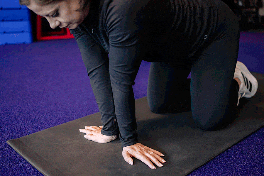 Anytime Fitness Coach demonstrating how to do a side-to-side rocking wrist stretch.