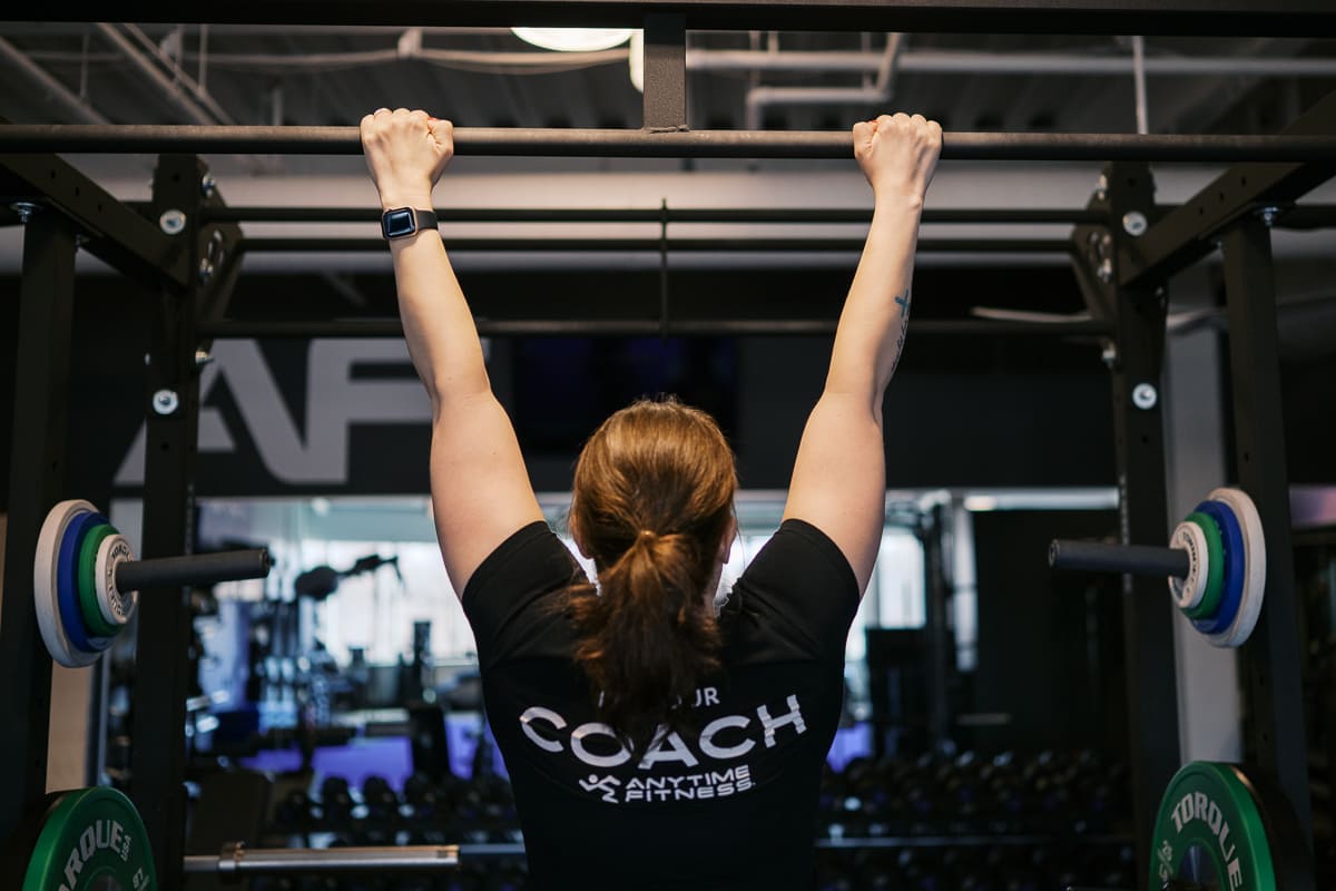 Anytime Fitness Coach demonstrating how to do a dead hang.