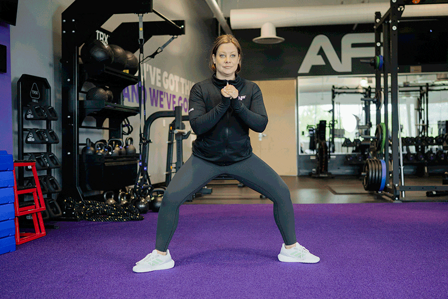 Anytime Fitness Coach demonstrating a sumo squat mobility stretch.