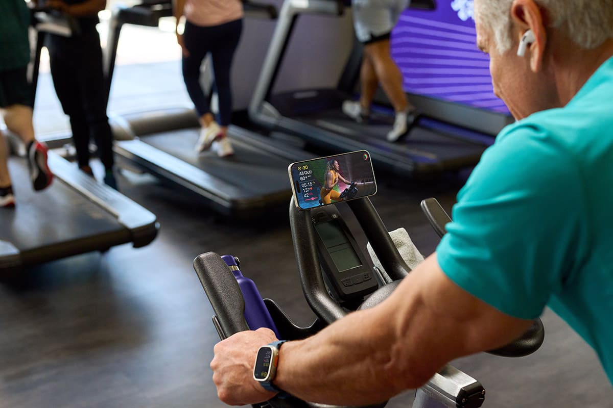A man is working out on a stationary bike while listening to and watching a video guide to the workout on his smartphone.