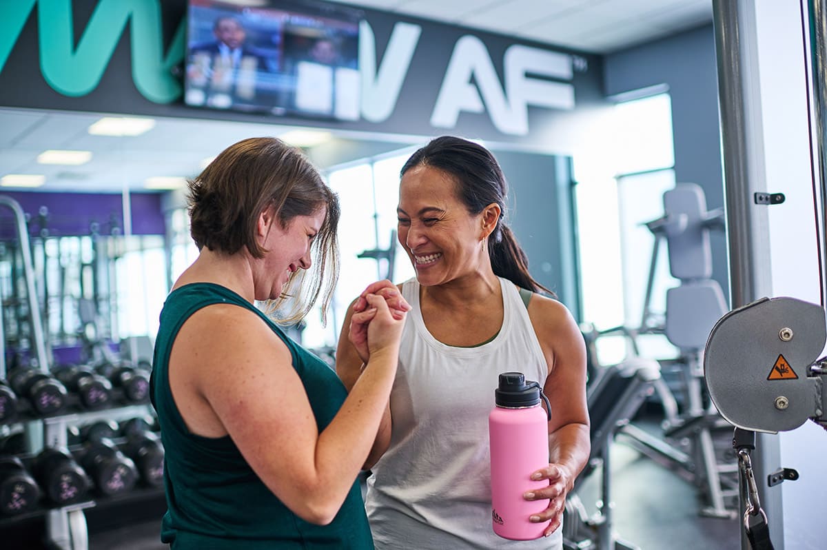 Two women are standing in an AF gym and smiling while congratulating each other for making progress with a handshake.