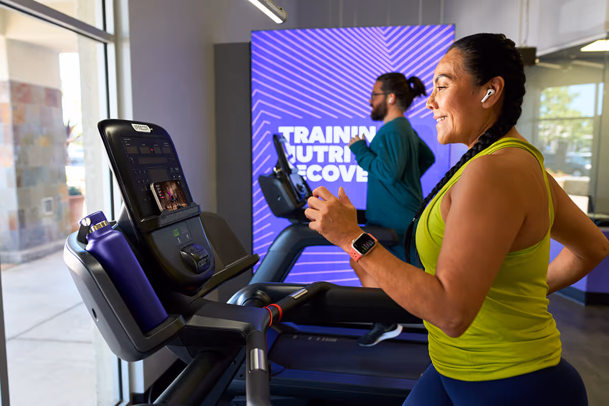A woman wearing headphones and a smart watch running on a treadmill while following an Apple Fitness+ guided treadmill workout.