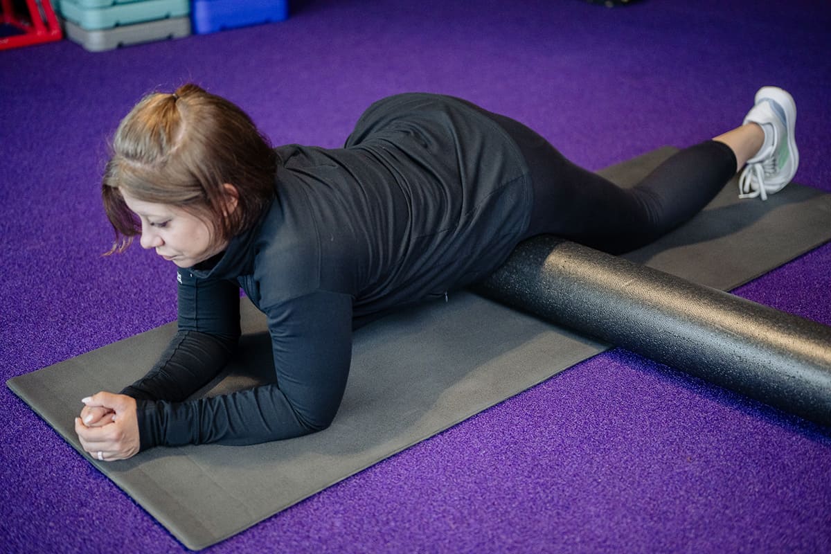 Anytime Fitness Coach demonstrating hip mobility exercises with a foam roller, stretching the hips.