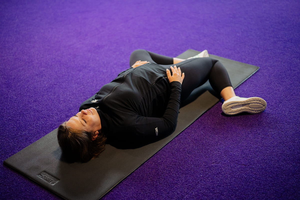 Anytime Fitness Coach demonstrating hip mobility exercises, including the static lying internal hip rotation stretch.
