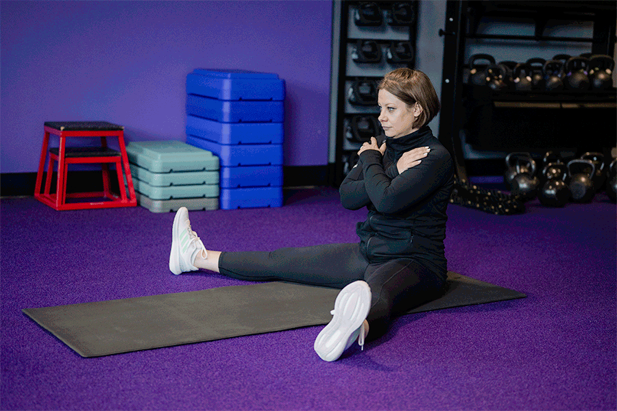 Anytime Fitness Coach demonstrating hip mobility exercises, including a seated straddle stretch.