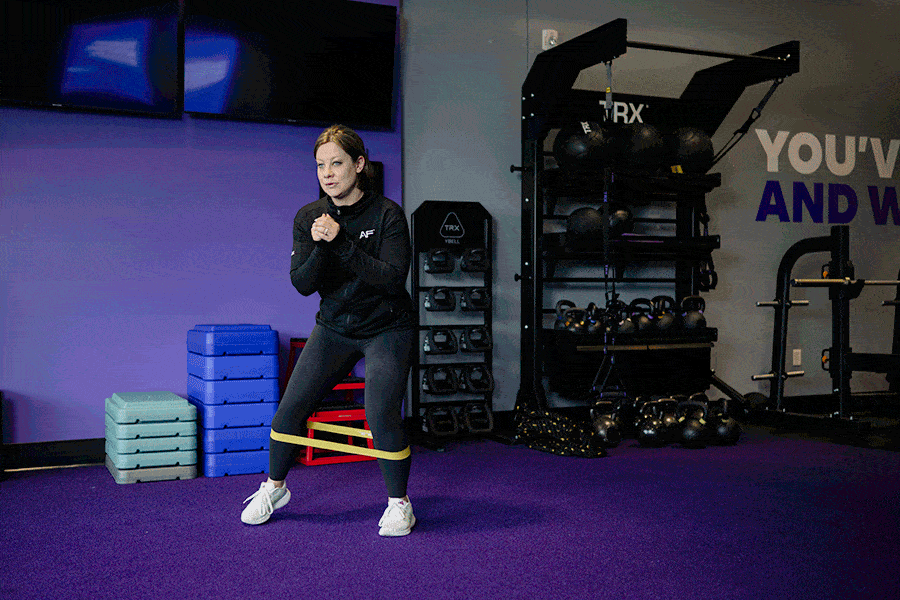 Anytime Fitness Coach demonstrating hip mobility exercises, including mini-band lateral steps.