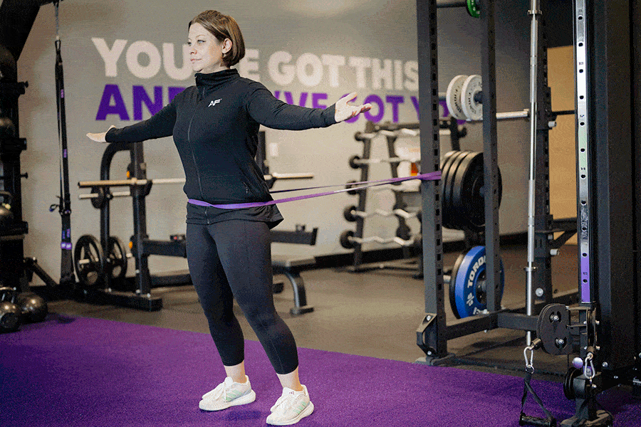 Anytime Fitness Coach demonstrating a modification for the split stance hip hinge, a band-resisted hip hinge.
