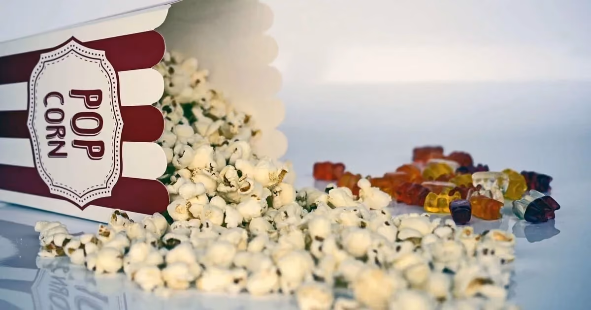 A striped popcorn box tipped over, popcorn spilling out alongside colorful gummy bears.