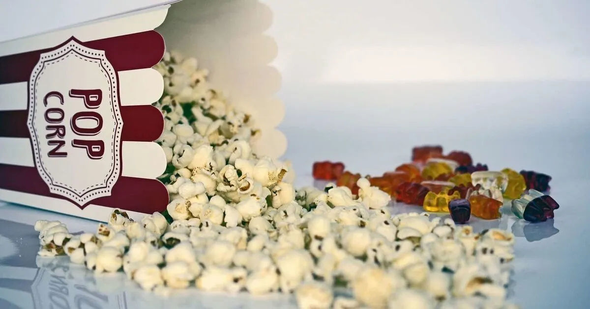 A striped popcorn box tipped over, popcorn spilling out alongside colorful gummy bears. 