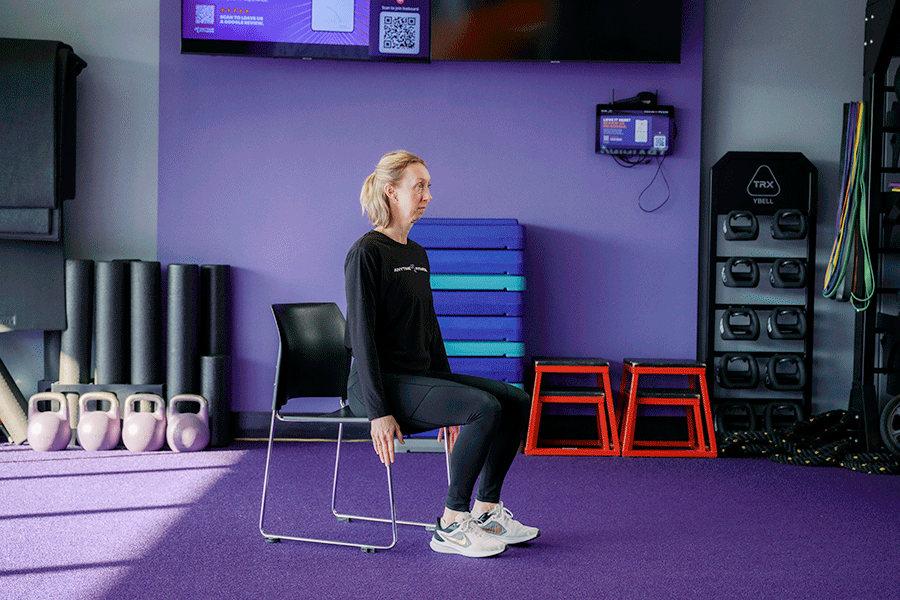 Anytime Fitness Coach demonstrating a sit-to-stand chair squat, a strength and balance exercise.