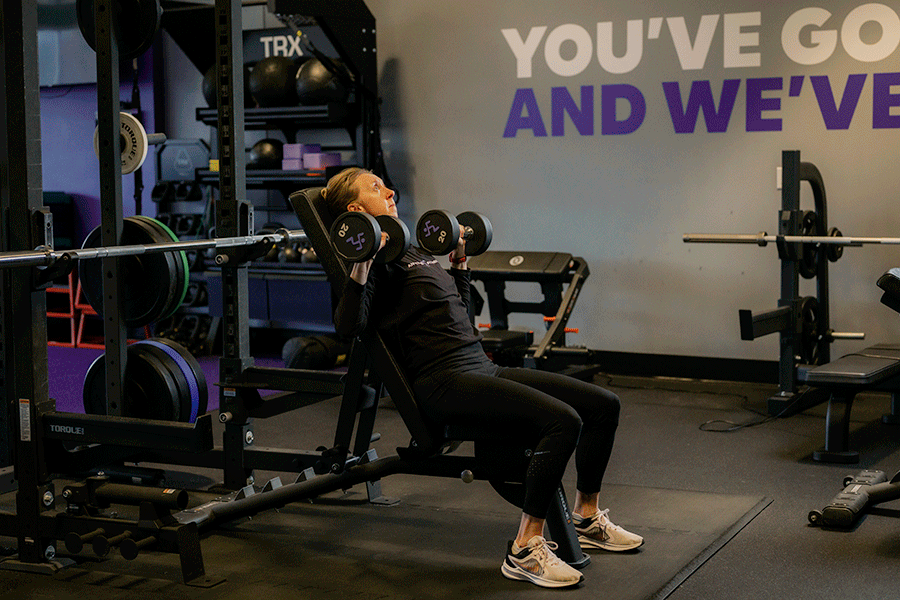 Anytime Fitness Coach demonstrating a seated overhead press with dumbbells.