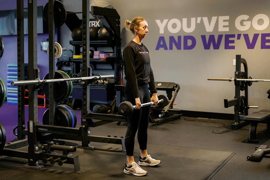 Anytime Fitness Coach demonstrating an upright row with a fixed barbell.