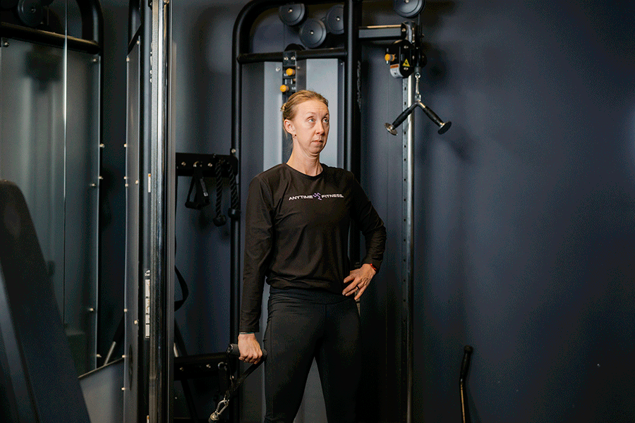 Anytime Fitness Coach demonstrating a single-arm cable front raise.