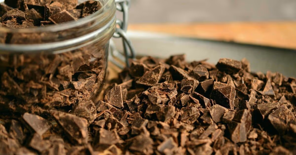 Close-up of dark chocolate chunks spilling from an open glass jar onto a wooden surface, creating a tempting and indulgent atmosphere.