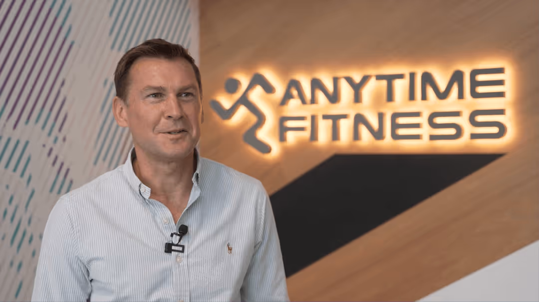 Anytime Fitness franchisee Guy Warner sharing his business ownership testimonial in front of a glowing brand logo.