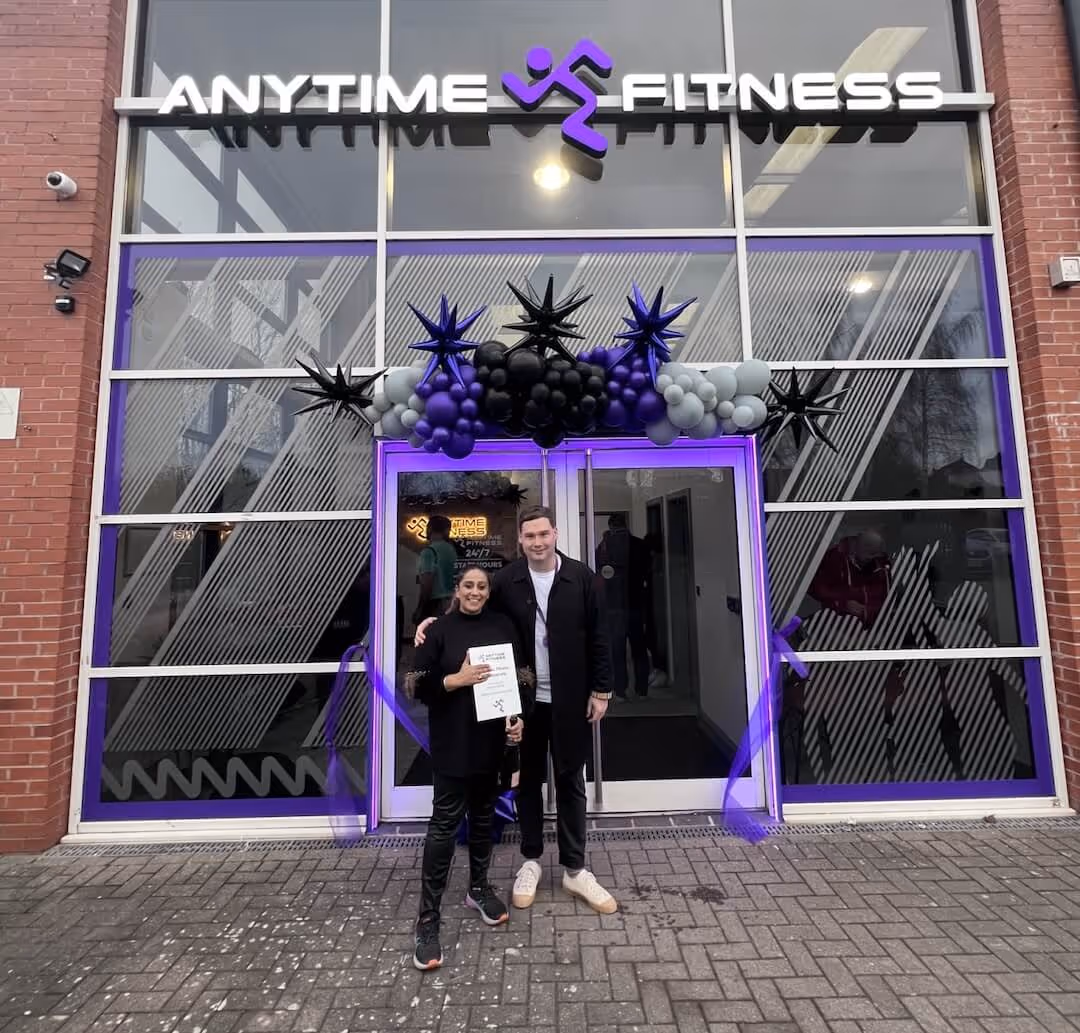 Franchise owner Sharon Thandi celebrating the grand opening of her new Anytime Fitness gym storefront with festive purple balloons.