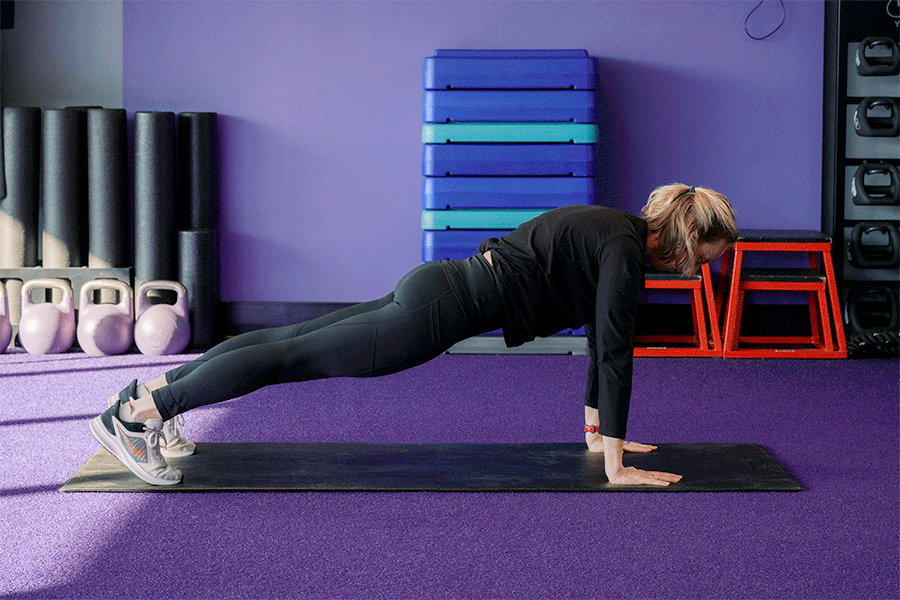 Anytime Fitness Coach demonstrating a plank to downward dog, part of a mobility strength training workout.