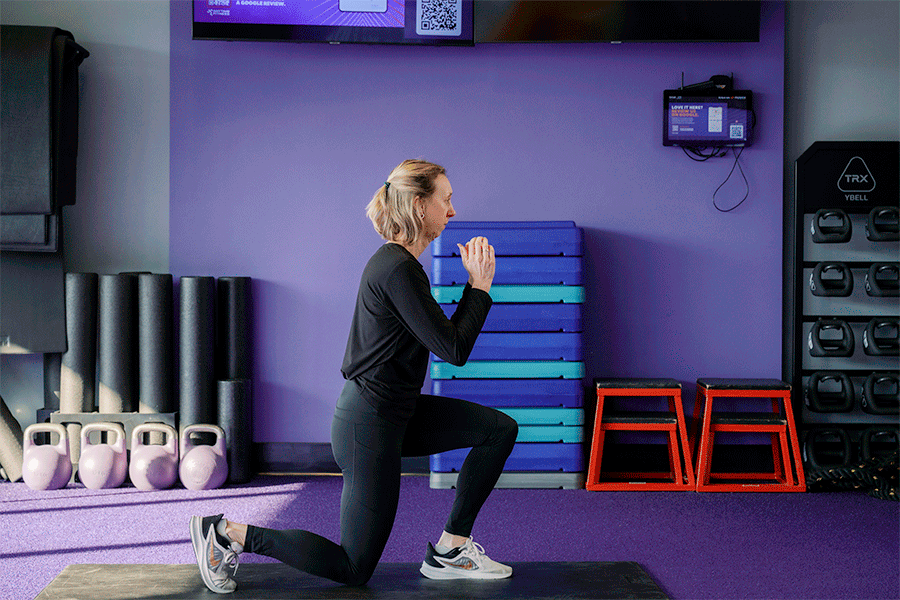 Anytime Fitness Coach demonstrating a reverse lunge with a knee drive, part of a mobility strength training workout.