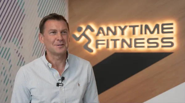Anytime Fitness franchisee Guy Warner sharing his business ownership testimonial in front of a glowing brand logo.
