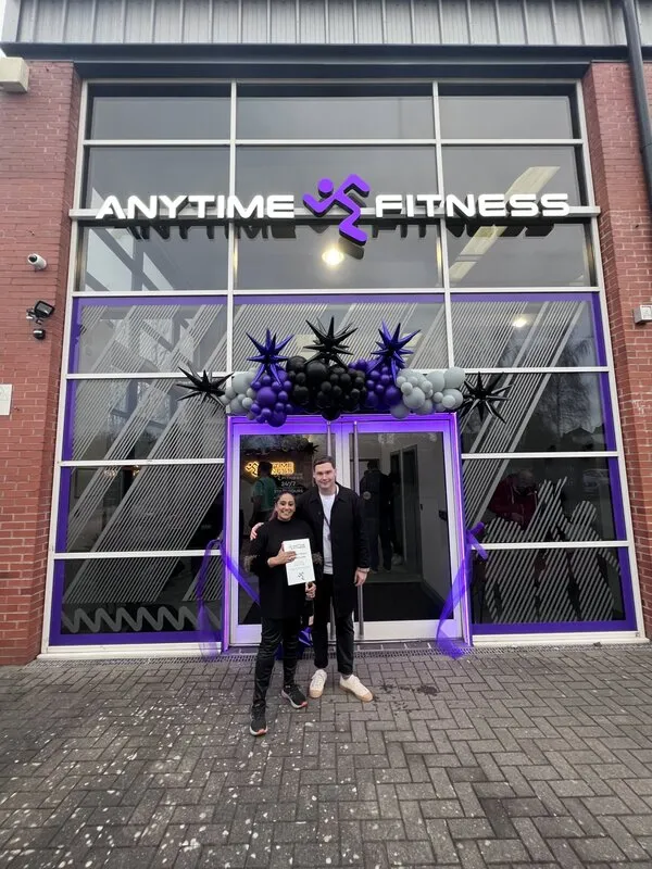 Franchise owner Sharon Thandi celebrating the grand opening of her new Anytime Fitness gym storefront with festive purple balloons.
