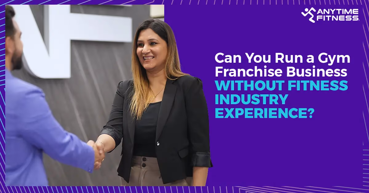 A professional woman in business attire smiling and shaking hands with a colleague in front of an Anytime Fitness logo, illustrating a successful gym franchise partnership.