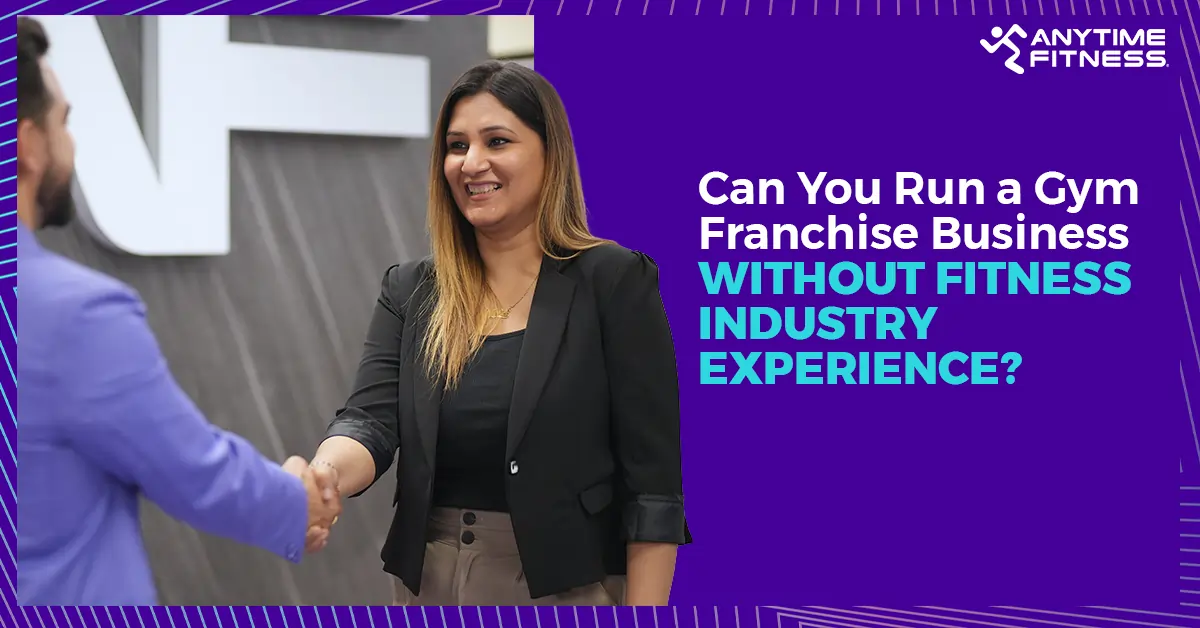 A professional woman in business attire smiling and shaking hands with a colleague in front of an Anytime Fitness logo, illustrating a successful gym franchise partnership.
