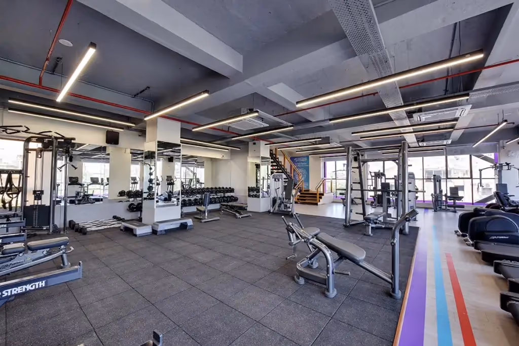 A wide-angle view of a modern, well-equipped Anytime Fitness gym floor featuring strength training machines, a dumbbell rack, power racks, and cardio equipment in a clean, professional setting.