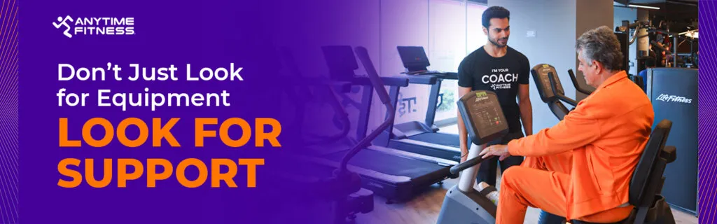 Promotional banner titled "Don't Just Look for Equipment, Look for Support." The image shows a professional fitness coach wearing an "I'm Your Coach" shirt assisting an older man on a stationary exercise bike.