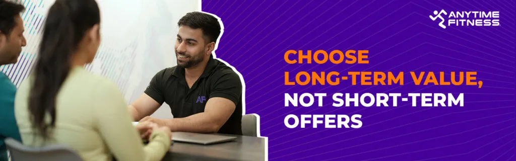 A banner with the heading "Choose Long-Term Value, Not Short-Term Offers." The left side shows a gym consultant in a black "AF" branded polo shirt smiling while speaking with a couple during a professional consultation.