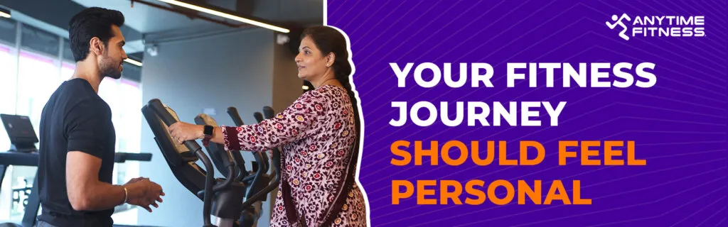 Anytime Fitness banner titled "Your Fitness Journey Should Feel Personal." The image depicts a male trainer having a one-on-one conversation with a woman using a cardio machine, highlighting personalized attention.