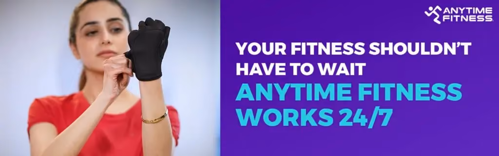 Promotional banner titled "Your Fitness Shouldn’t Have To Wait, Anytime Fitness Works 24/7." The image features a woman in a red shirt focused on adjusting her black weightlifting gloves, emphasizing the readiness to train at any hour.