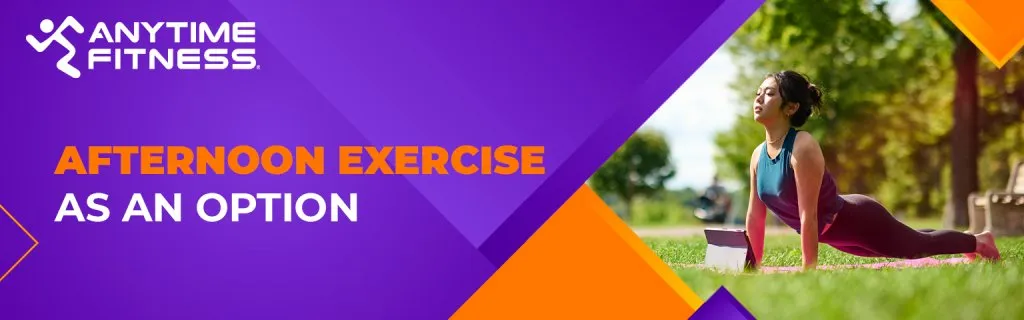 A promotional banner with the text "AFTERNOON EXERCISE AS AN OPTION." The image features a woman practicing an upward-facing dog yoga pose on a pink mat in a sunlit park, using a tablet for guidance.