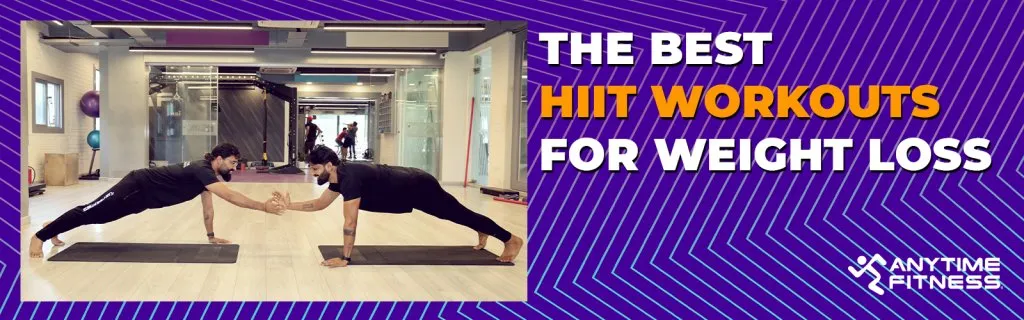 Anytime Fitness blog banner titled "THE BEST HIIT WORKOUTS FOR WEIGHT LOSS." The visual shows two men facing each other in high plank positions on yoga mats, performing a partner-based exercise by high-fiving in a spacious, modern gym.