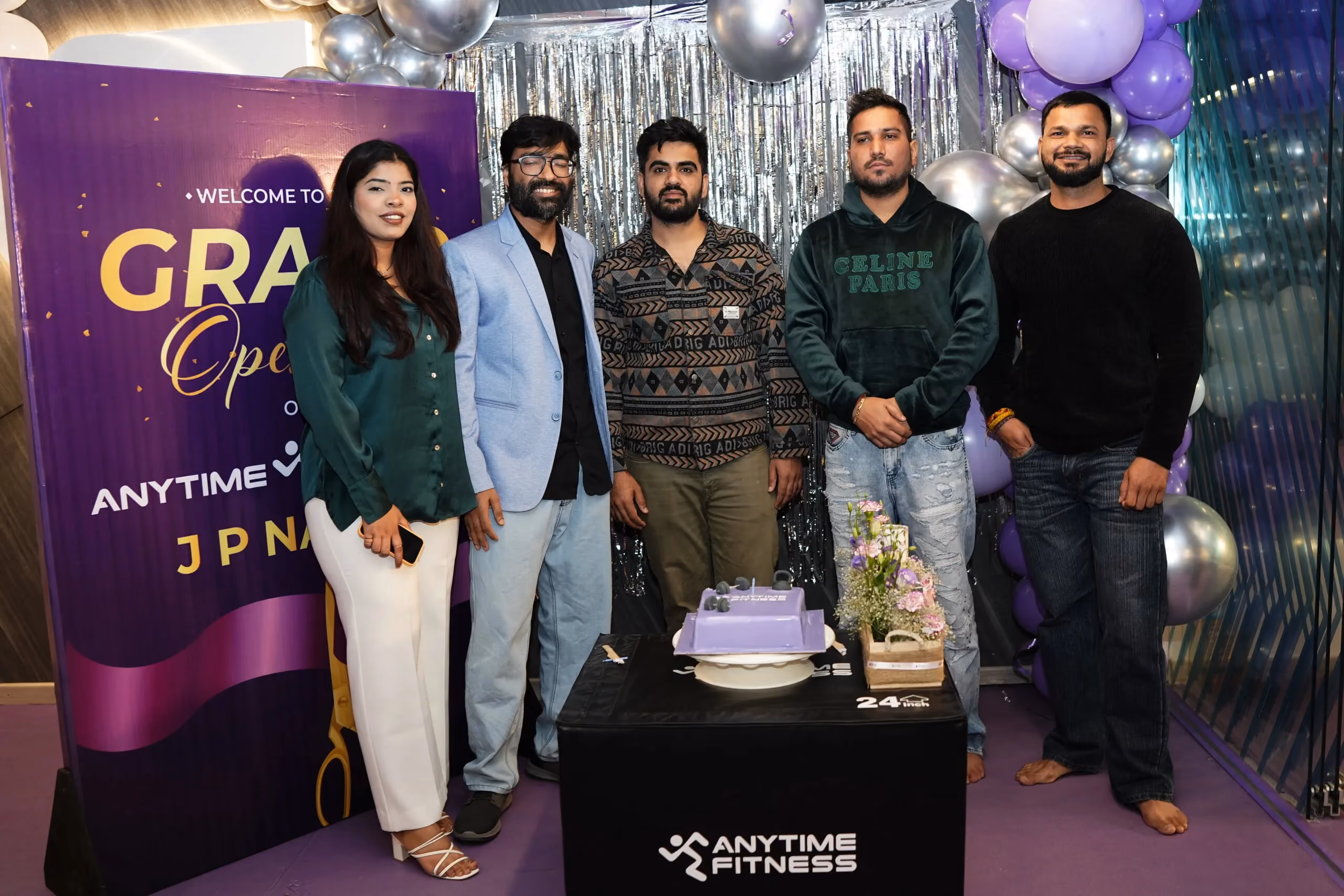 Group of Anytime Fitness team members and guests at a grand opening event in JP Nagar, posing beside branded signage, balloons, and celebration cake.