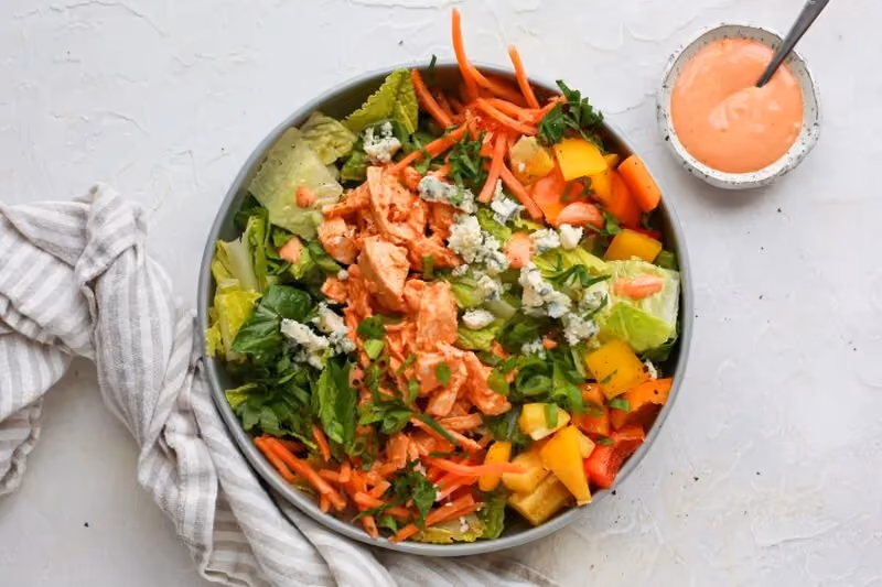 Creamy buffalo chicken salad bowl, a high-fiber, high-protein meal with carrots, peppers, lettuce, chicken, and blue cheese.