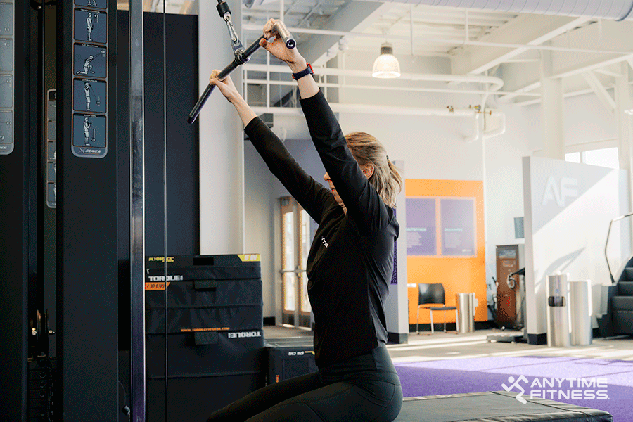 Anytime Fitness Coach demonstrating a lat pulldown, a cable machine exercise.