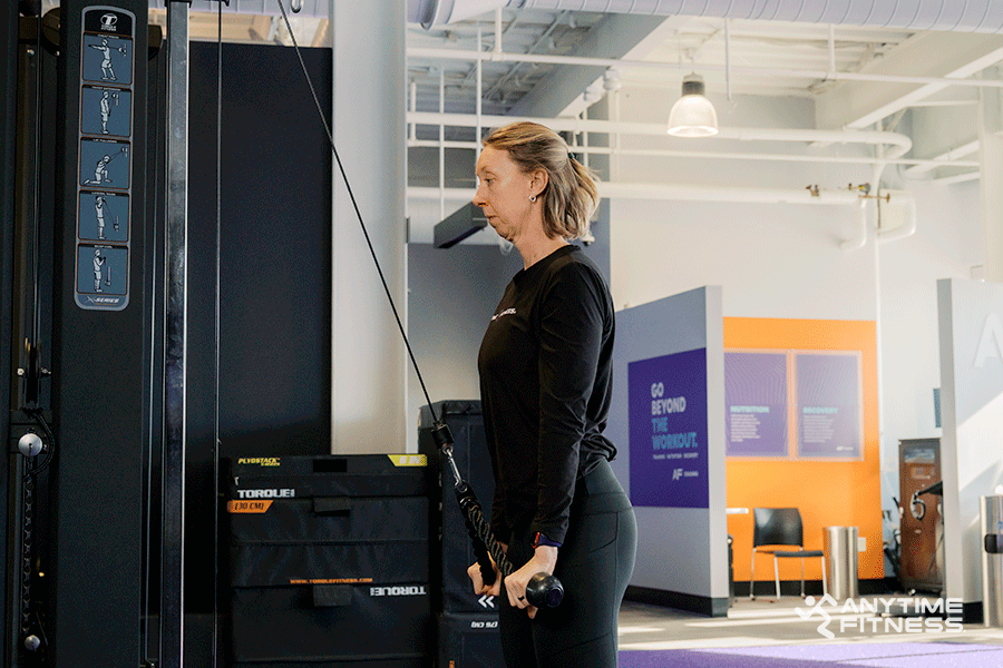 Anytime Fitness Coach demonstrating a tricep rope extension, a cable machine exercise.