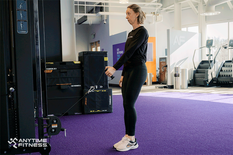 Anytime Fitness Coach demonstrating a cable machine exercise with a lunge movement.