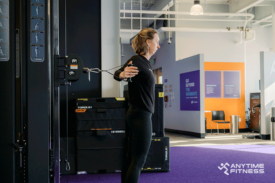 Anytime Fitness Coach demonstrating a chest fly, a cable machine exercise.