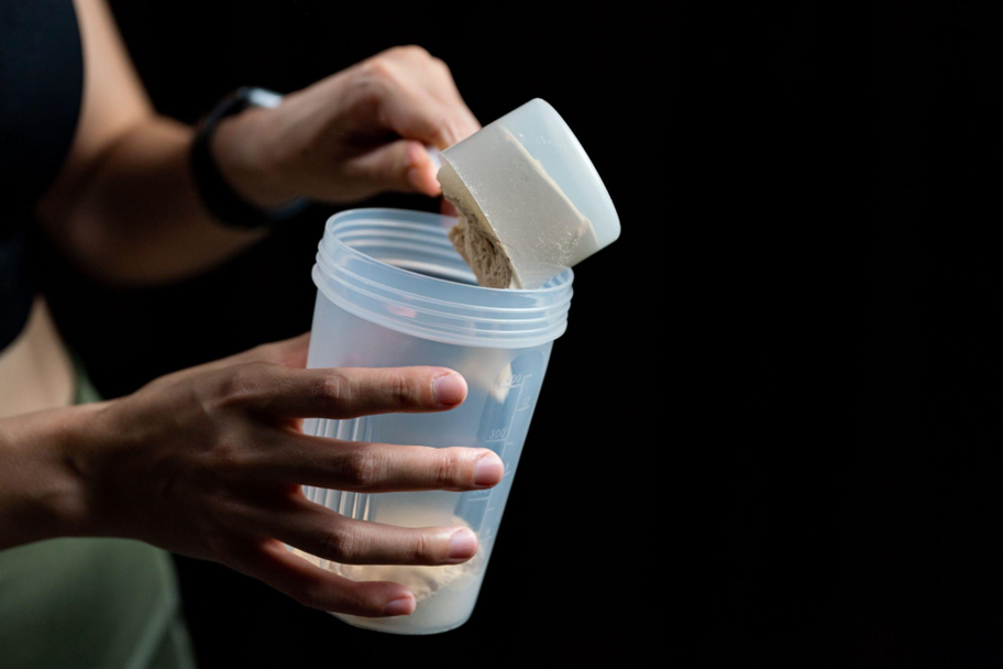 Person mixing a protein powder into a blender bottle.