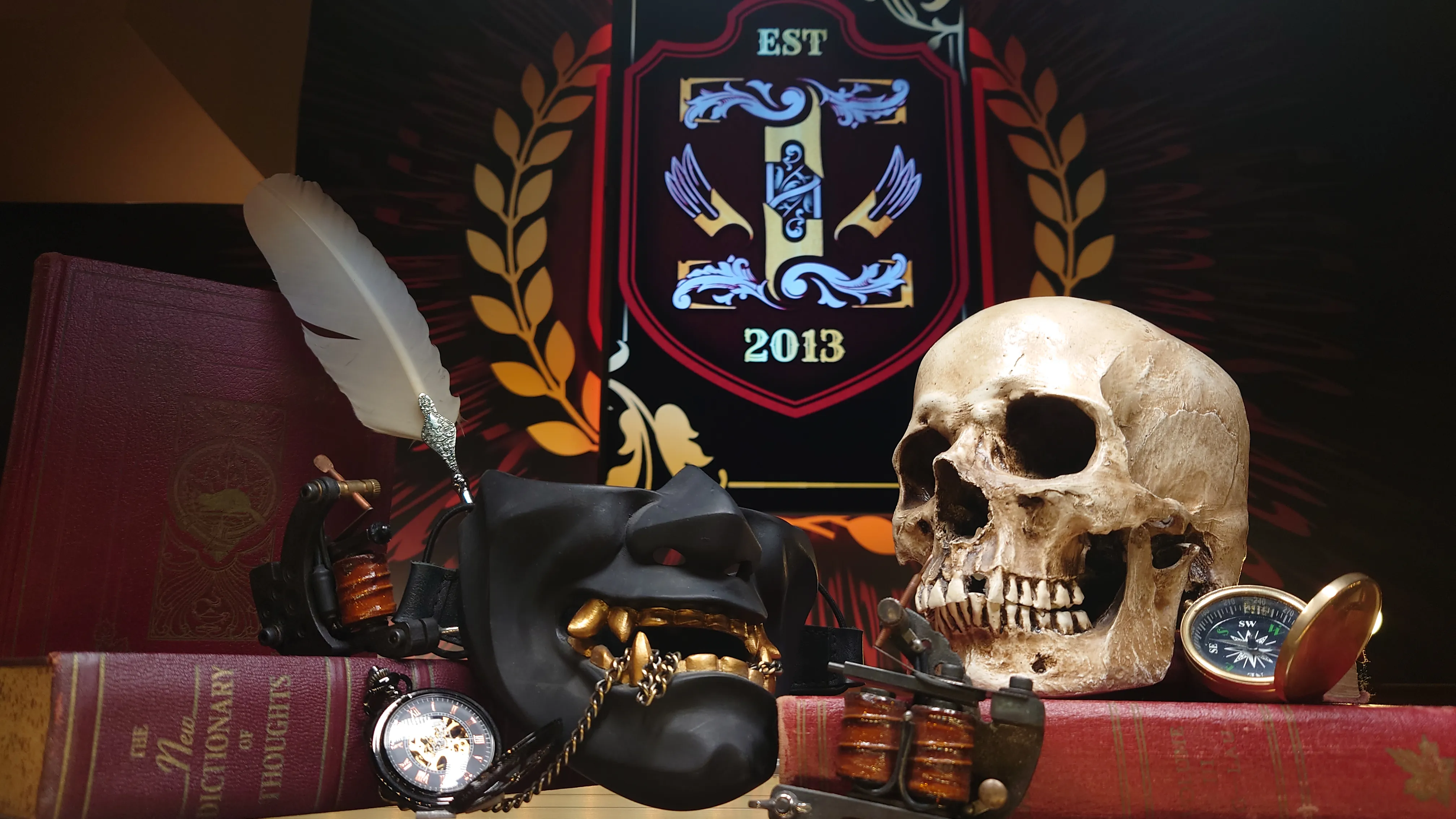 Ink Well crest with a skull, tattoo machine and books