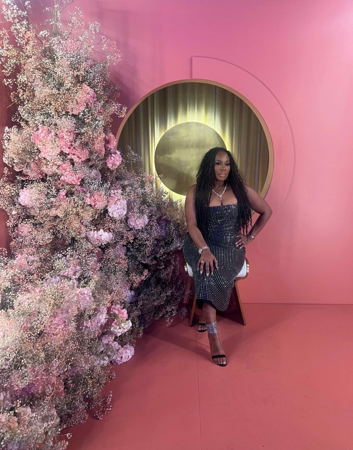 Dr. Topeka K. Sam standing beside a floral installation in a pink room.